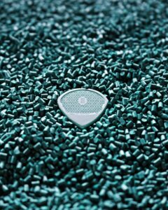 Close-up of a blue guitar pick resting on a bed of turquoise plastic pellets, showcasing texture and detail.