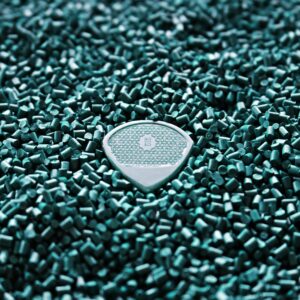 Close-up of a blue guitar pick resting on a bed of turquoise plastic pellets, showcasing texture and detail.