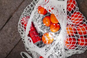 A net bag filled with fresh oranges and a soda can, adorned with LED lights on a textured surface.