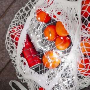 A net bag filled with fresh oranges and a soda can, adorned with LED lights on a textured surface.