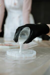 Close-up of black-gloved hand pouring resin into mold, showcasing craftsmanship.