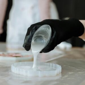 Close-up of black-gloved hand pouring resin into mold, showcasing craftsmanship.
