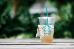 Close-up of an iced drink in a disposable Starbucks cup on a wooden table outdoors.
